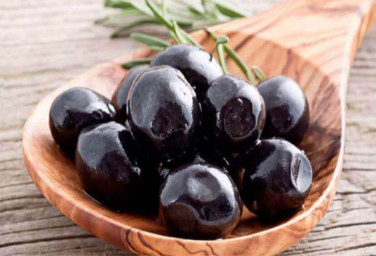 Black olives in sunflower oil with spices on a wooden spoon.