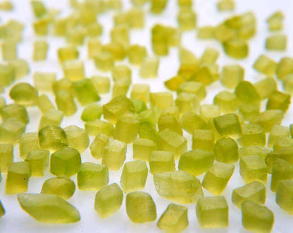 Close-up of small, green rough peridot gemstones scattered on a white surface.