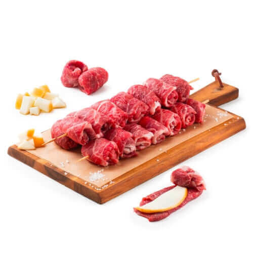 Raw beef skewers with cheese cubes and lemon slice on a wooden cutting board with sea salt.