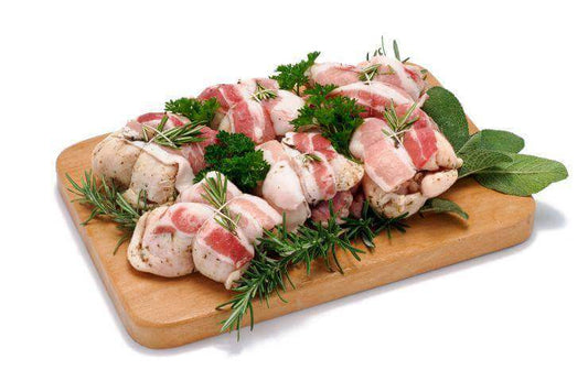 Bacon-wrapped chicken breasts garnished with fresh herbs on a wooden cutting board.