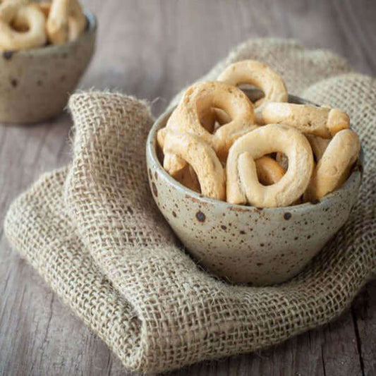 Rustic bowl filled with traditional Italian taralli biscuits on a textured burlap cloth.